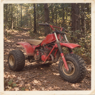 Vintage 1980s red three-wheeler ATV on a forest trail, retro off-road stock photo with faded film texture.